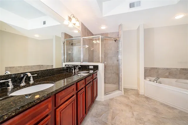 a spacious bathroom with a granite countertop double vanity sink a mirror and a bathtub