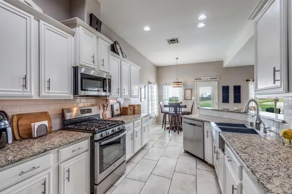 a kitchen with stainless steel appliances granite countertop a stove top oven a sink a dining table and chairs