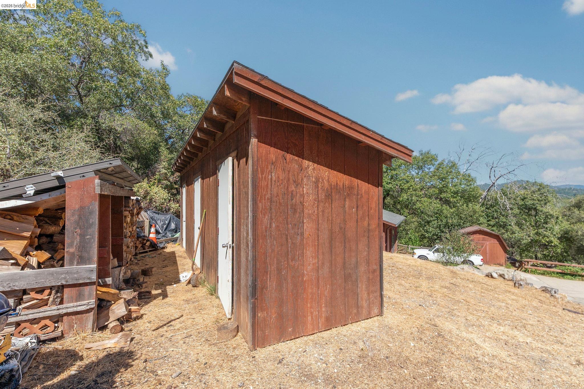 22963 Robertson Ranch Road Sonora, CA 95370 - Photo 70 of 90 Red-stained wood shed with white doors, featuring a sloped roof and exposed rafters