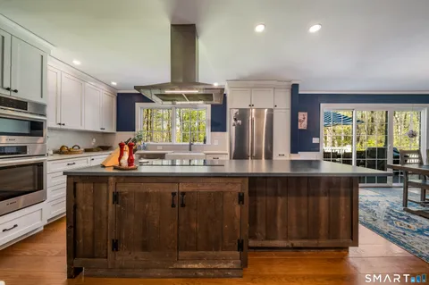 a kitchen with stainless steel appliances granite countertop a stove a sink dishwasher a refrigerator and a dining table with wooden floor