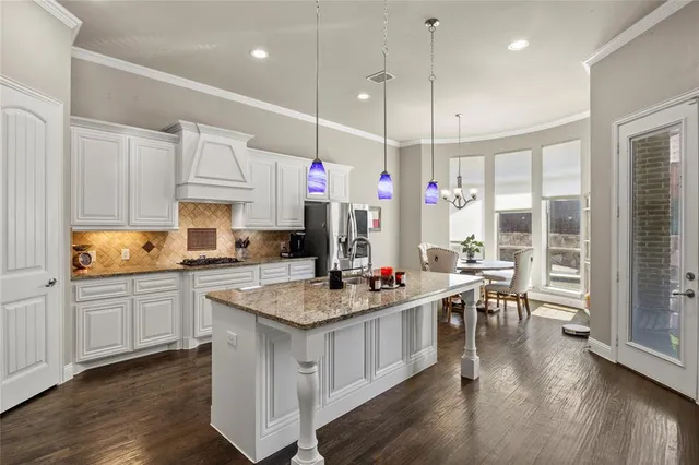 a kitchen with kitchen island granite countertop a stove a sink a dining table and chairs with wooden floor