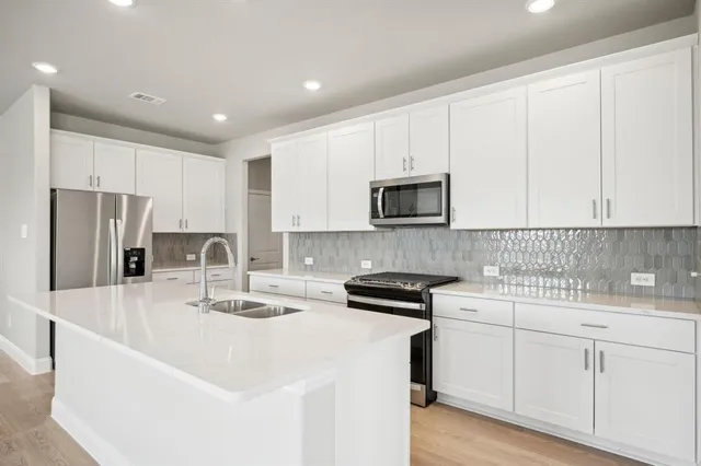 a kitchen with stainless steel appliances granite countertop a sink a stove a refrigerator and white cabinets