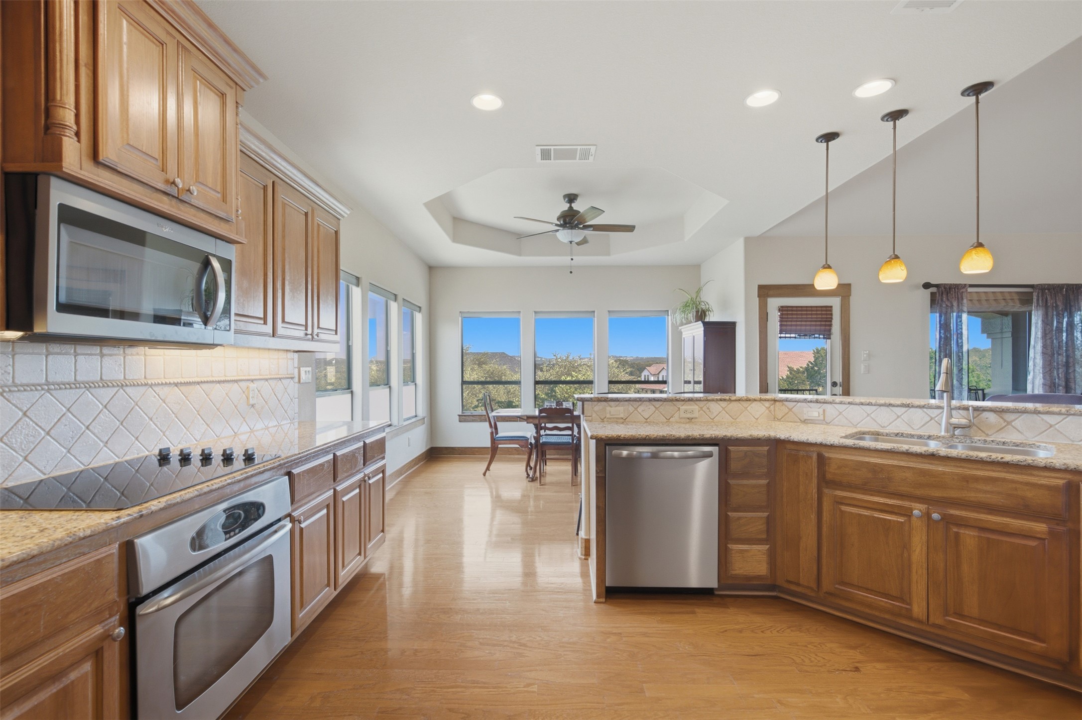 700 Augusta Circle Point Venture, TX 78645 - Photo 6 of 35 A warm kitchen with hardwood floors, natural wood cabinetry, and a tray ceiling, illuminated by recessed lighting and pendant fixtures.