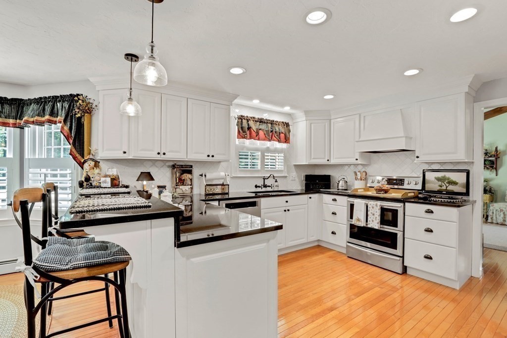a kitchen with stainless steel appliances granite countertop a stove top oven a sink a dining table and chairs with white cabinets