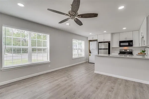 a view of kitchen with stainless steel appliances granite countertop a stove a sink a refrigerator with white cabinets and wooden floor