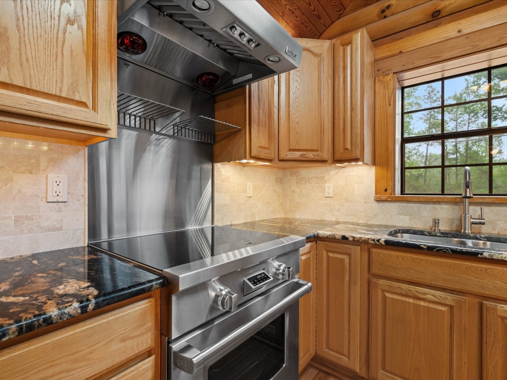 12868 Levi Road Willis, TX 77378 - Photo 13 of 41 High-end kitchen featuring a premium Wolf range and vent hood, complemented by granite countertops and warm wood cabinetry.