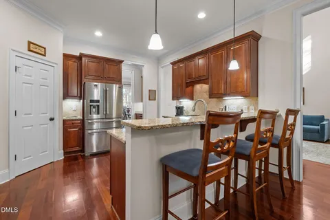 a open kitchen with stainless steel appliances granite countertop a stove top oven a refrigerator a dining table and chairs with wooden floor