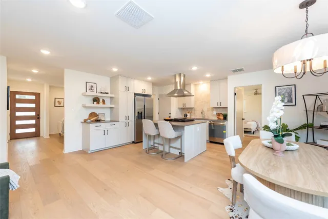 a living room with stainless steel appliances kitchen island granite countertop a table chairs and a refrigerator