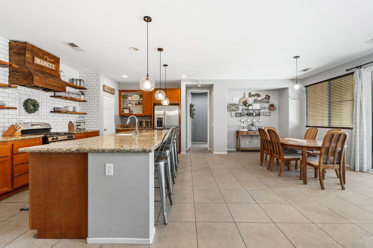 42724 Tango Court Indio, CA 92203 - Photo 6 of 27 a open kitchen with stainless steel appliances granite countertop a stove top oven a sink a dining table and chairs with the wooden floor