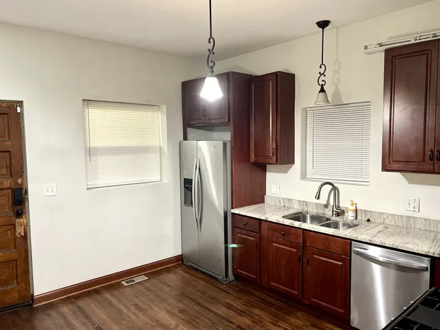 a kitchen with stainless steel appliances granite countertop a refrigerator a sink and a wooden floor