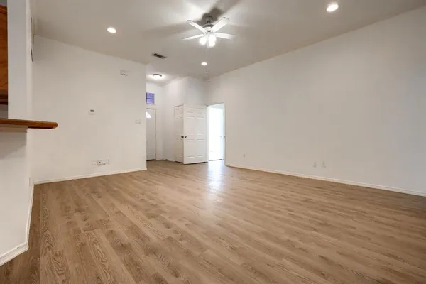 a view of an empty room with wooden floor and a ceiling fan