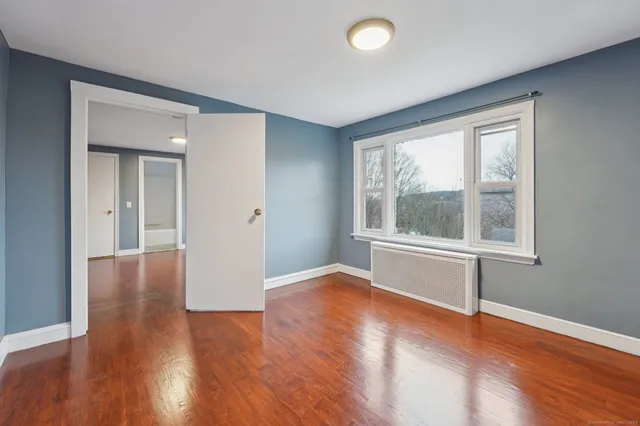 a view of an empty room with wooden floor and a window