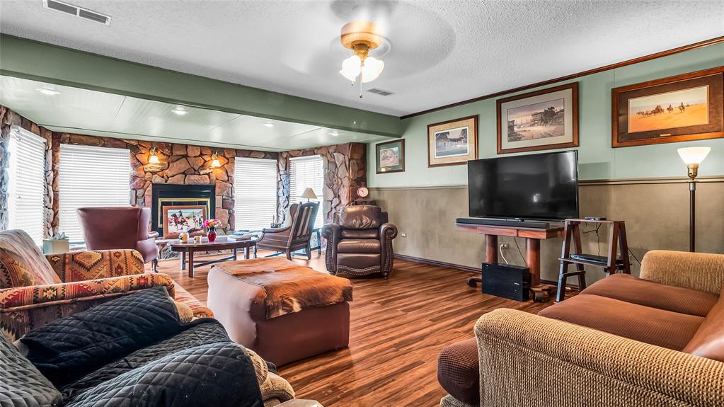 193 Eisenhower Road Denison, TX 75020 - Photo 3 of 30 Living area featuring wainscoting, a stone fireplace, wood finished floors, a textured ceiling, and ceiling fan
