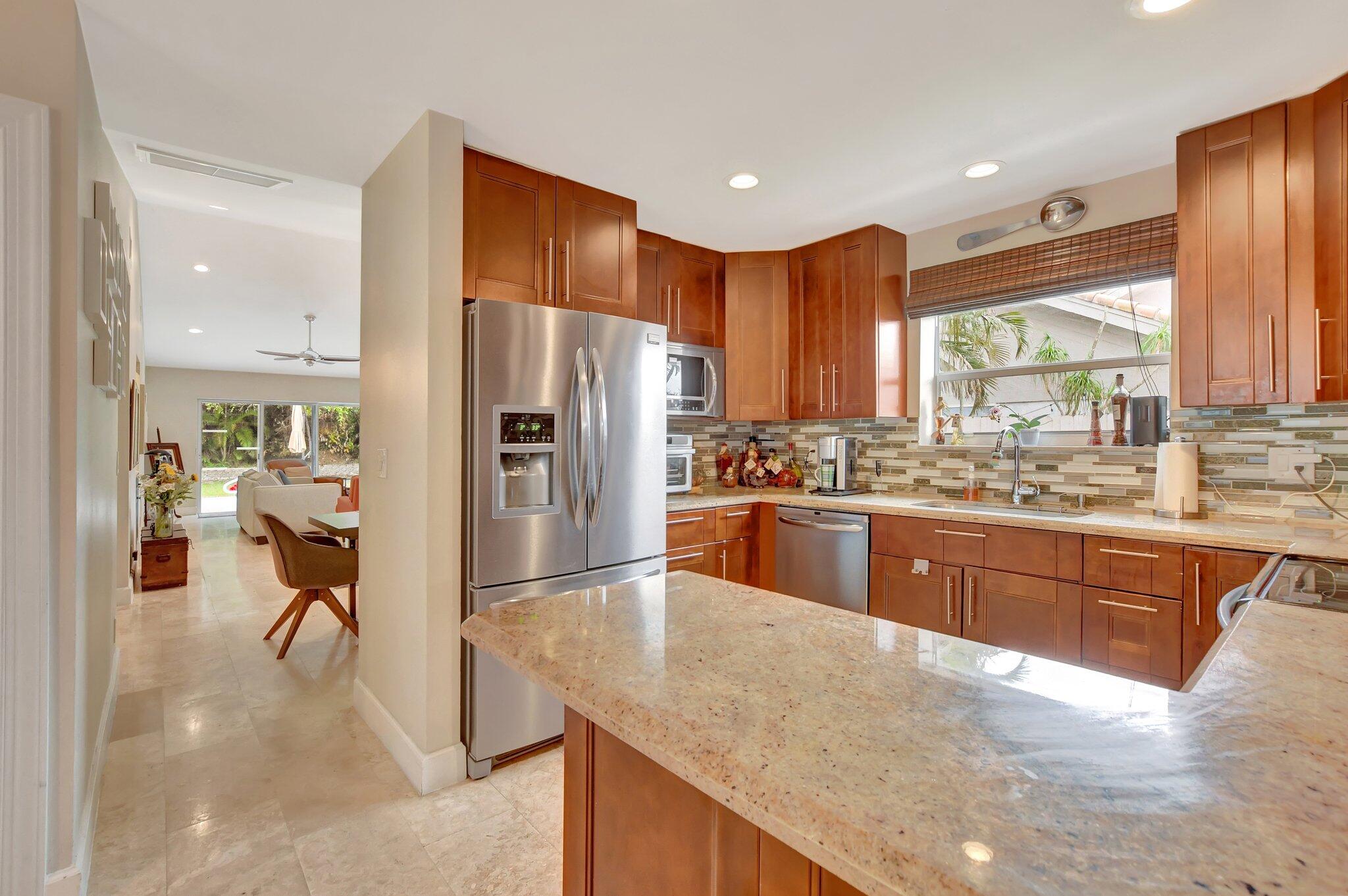 9717 Erica Court Boca Raton, FL 33496 - Photo 30 of 49 a kitchen with stainless steel appliances granite countertop a refrigerator a sink a stove with wooden cabinets and wooden floor