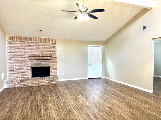 a view of an empty room with wooden floor fireplace and a window