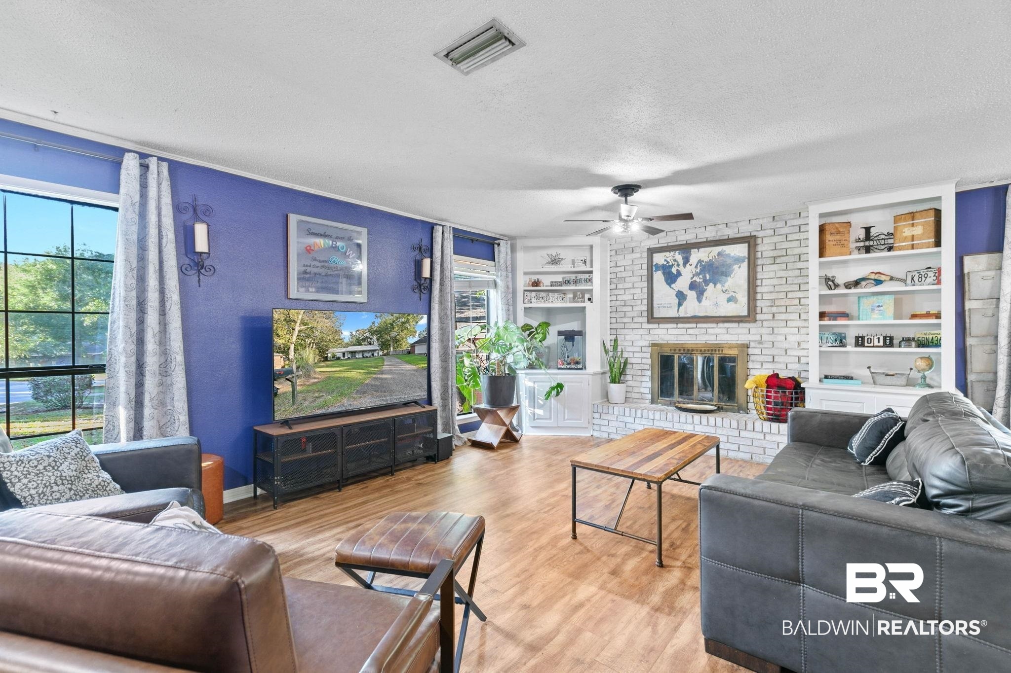 Living area with wood finished floors, a textured ceiling, built in features, a ceiling fan, and a brick fireplace