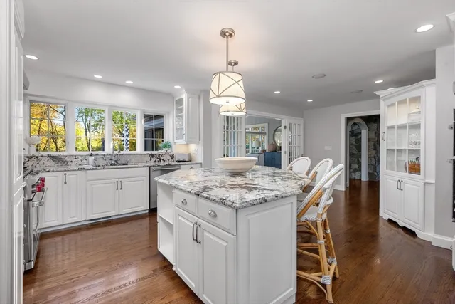 a kitchen with stainless steel appliances granite countertop a kitchen island a stove a sink a refrigerator and a dining table with wooden floor