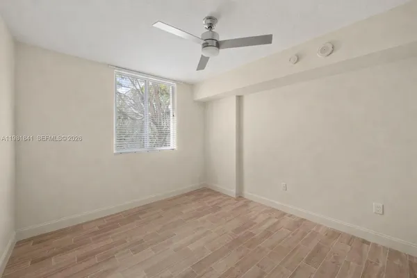 an empty room with wooden floor ceiling fan and windows
