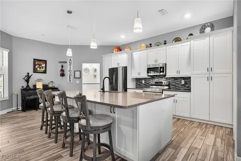 a kitchen with stainless steel appliances a white refrigerator a microwave a stove and white cabinets with wooden floor