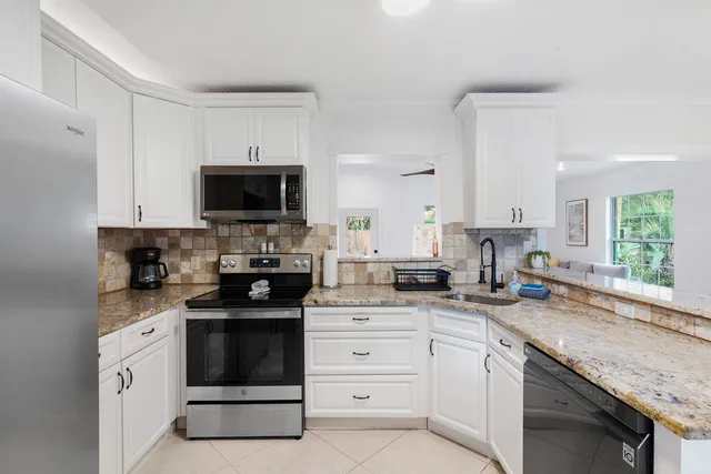 a kitchen with white cabinets appliances a sink and a window