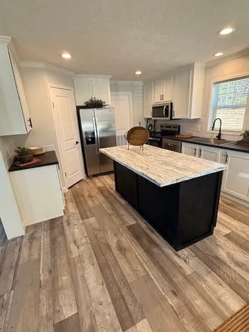 a large kitchen with stainless steel appliances kitchen island granite countertop a stove a refrigerator a sink and dishwasher with wooden floor