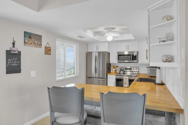 a living room with stainless steel appliances furniture a chandelier and a kitchen view