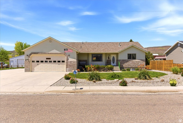 72 Canal Bank Road Garland, UT 84312 - Photo 2 of 40 Ranch-style residence featuring a two-car garage, concrete driveway, stone accents, a fenced yard, and landscaped front gardens