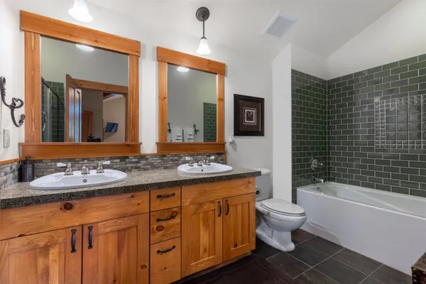 a bathroom with a double vanity sink a toilet a mirror and bathtub