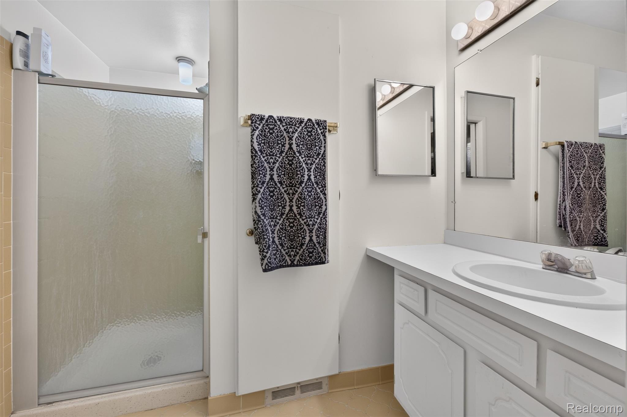 1439 Oakbrook E Drive Rochester, MI 48307 - Photo 38 of 68 Frosted glass shower enclosure, single vanity with integrated sink, wall-mounted mirror, and cabinet storage