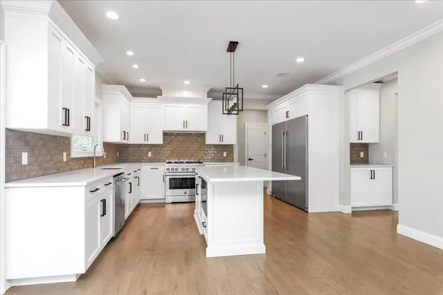 a large kitchen with stainless steel appliances kitchen island granite countertop a stove a sink a refrigerator and white cabinets with wooden floor