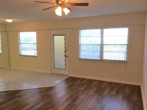 an empty room with wooden floor fan and windows