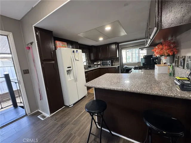 a kitchen with stainless steel appliances granite countertop a refrigerator a sink dishwasher a stove a dining table and chairs with wooden floor