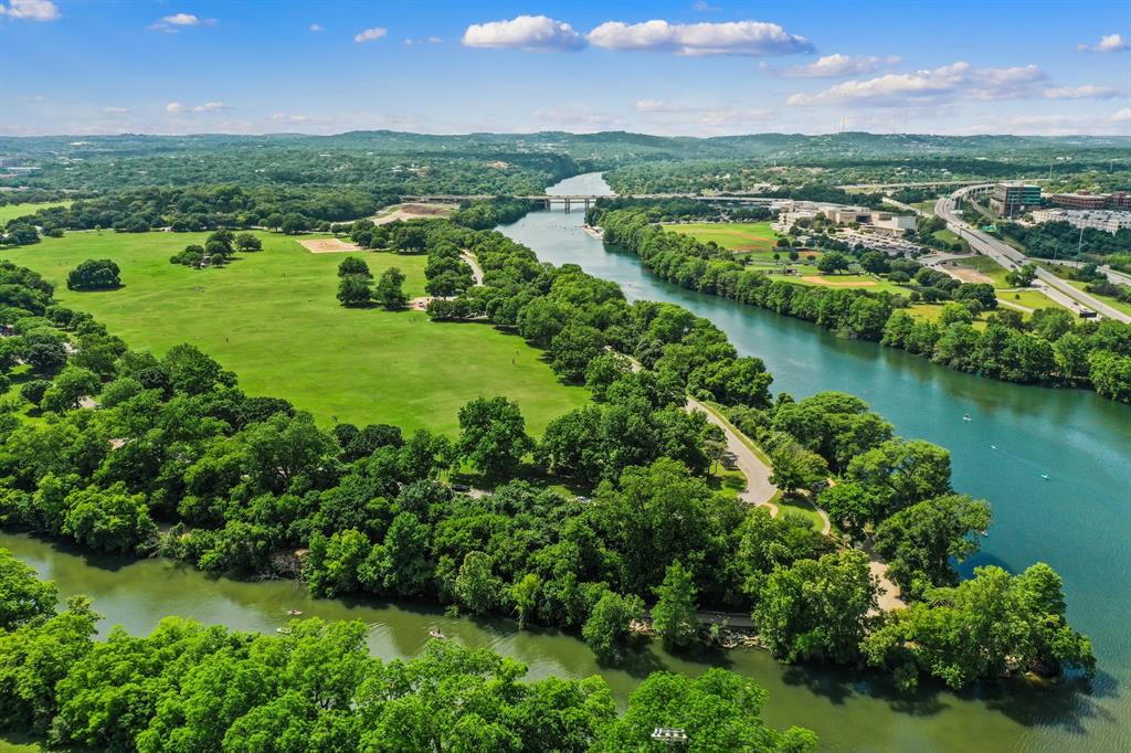 1900 Barton Springs Road, Unit 3013 Austin, TX 78704 - Photo 25 of 27 Lush green landscapes meet the calm waters of the river, bordered by a scenic roadway and distant bridge.