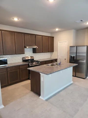 a kitchen with stainless steel appliances granite countertop a stove top oven a sink and a refrigerator with wooden floor