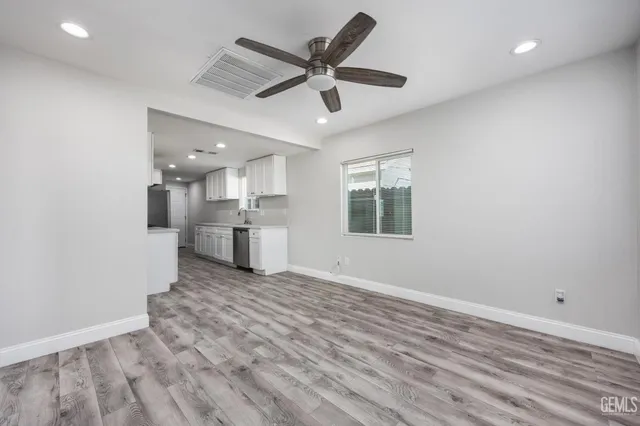 an empty room with wooden floor a ceiling fan and kitchen view