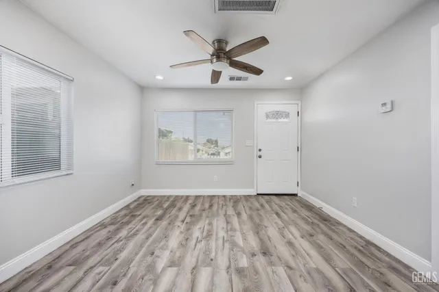 a view of an empty room with wooden floor and a ceiling fan