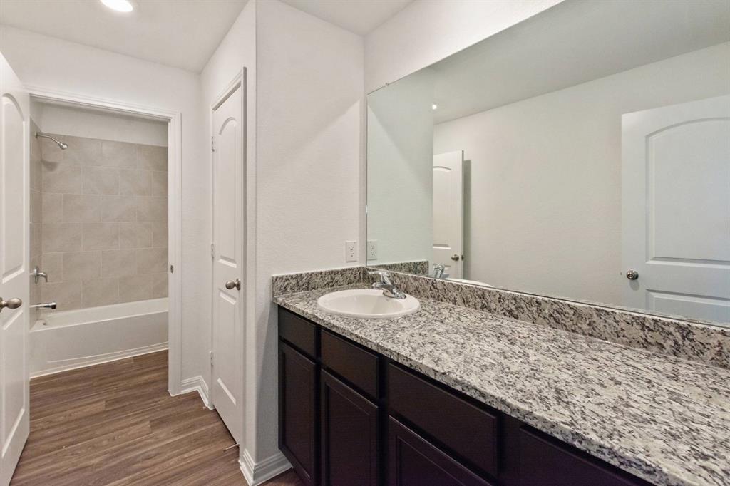 16429 Farmhouse Lane Elgin, TX 78621 - Photo 20 of 22 Bathroom vanity featuring a speckled countertop, integrated sink, and dark wood-finish cabinetry