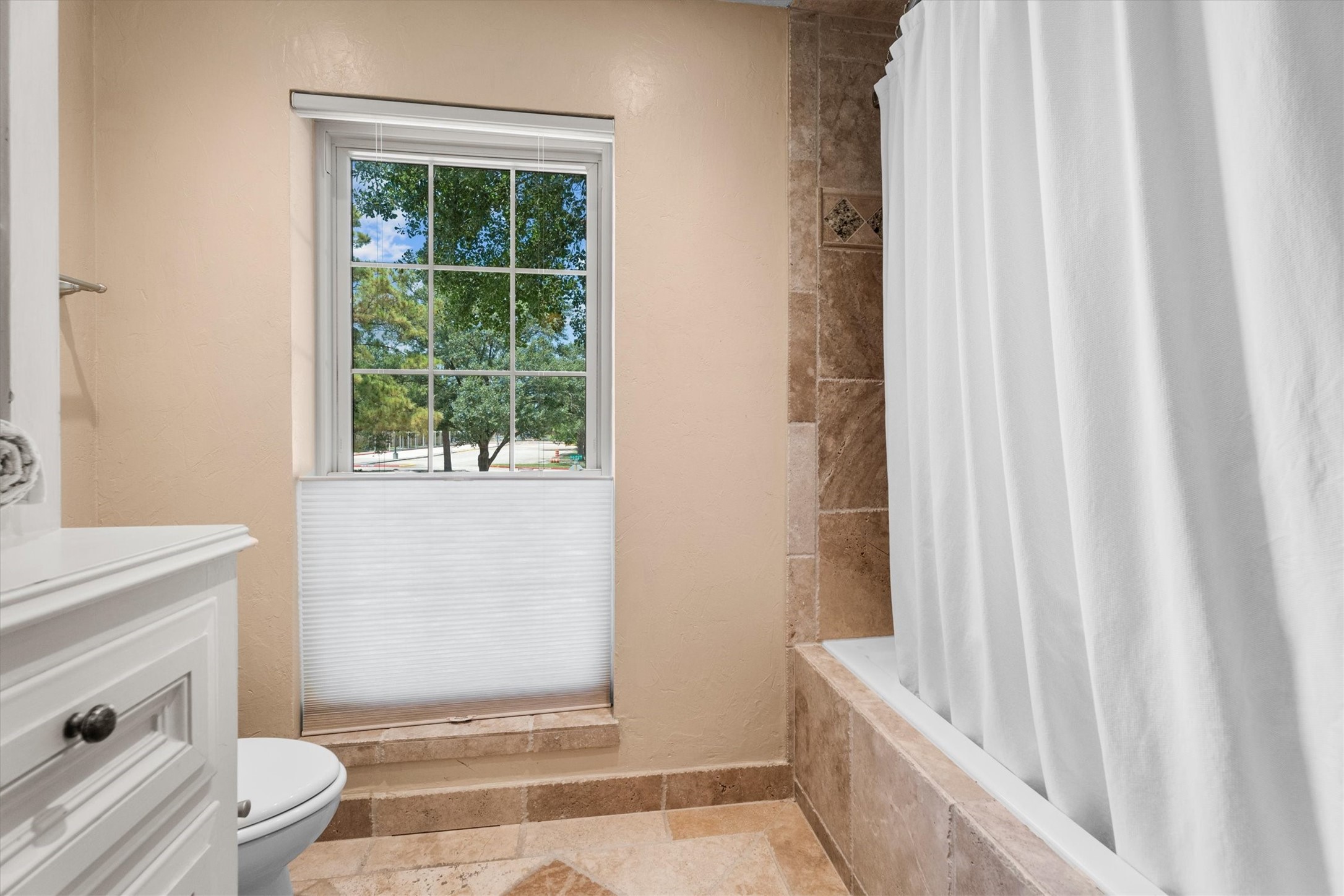 9103 Herts Road Spring, TX 77379 - Photo 34 of 46 A large window, with window covering, brightens the bathroom space. A large shower/tub combo is fully tiled, and an additional built-in cabinet with open shelving provides ample storage.