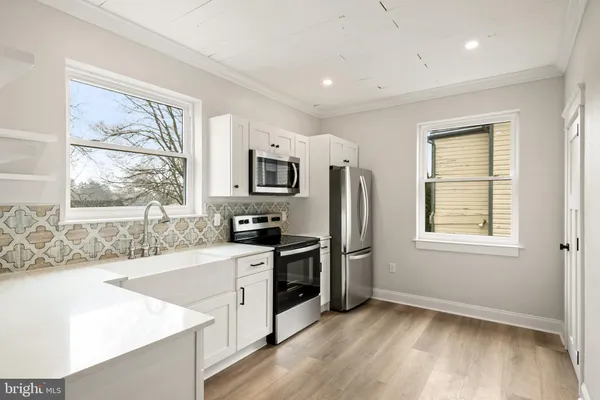 a kitchen with stainless steel appliances granite countertop a stove a sink a refrigerator white cabinets and wooden floor
