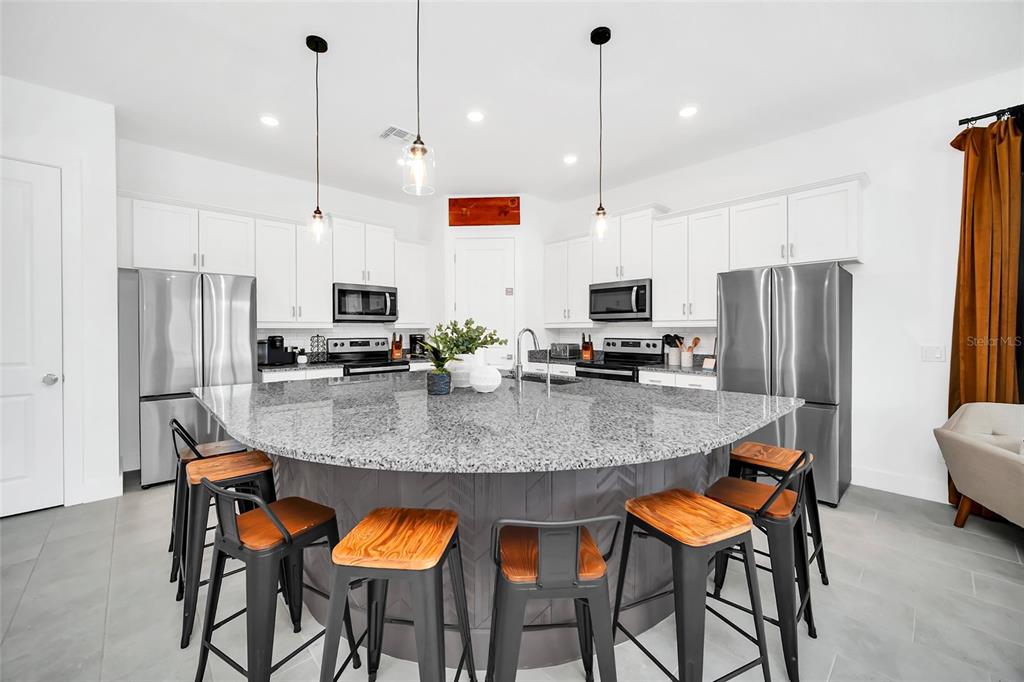 1213 Radiant Street Reunion, FL 34747 - Photo 27 of 84 a kitchen with stainless steel appliances granite countertop a stove a refrigerator a kitchen island a dining table and chairs