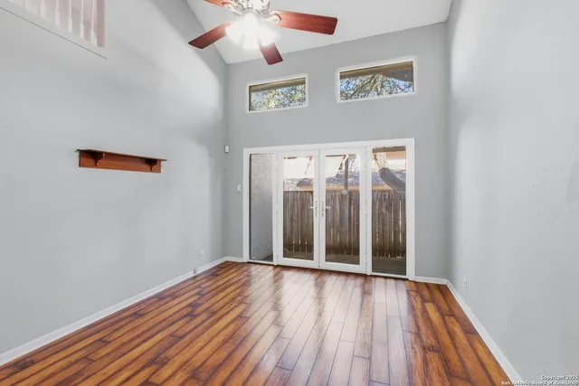 an empty room with wooden floor chandelier fan and windows