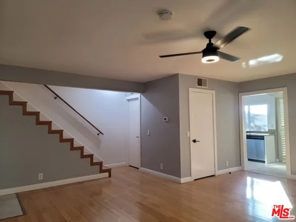 a view of an empty room with wooden floor and a ceiling fan