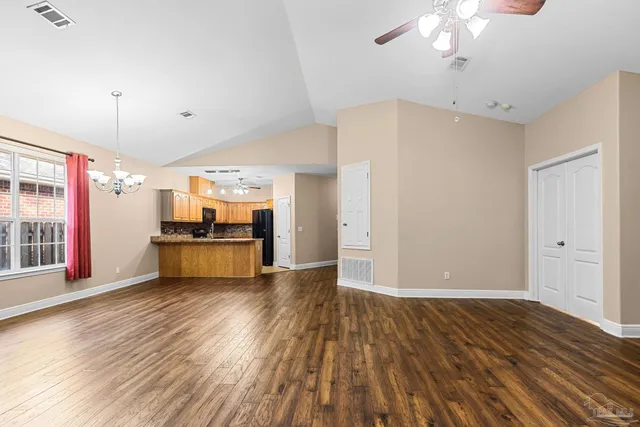 a view of an empty room with wooden floor and a kitchen