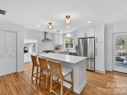 a kitchen with stainless steel appliances kitchen island granite countertop a refrigerator a stove a sink dishwasher and white cabinets with wooden floor