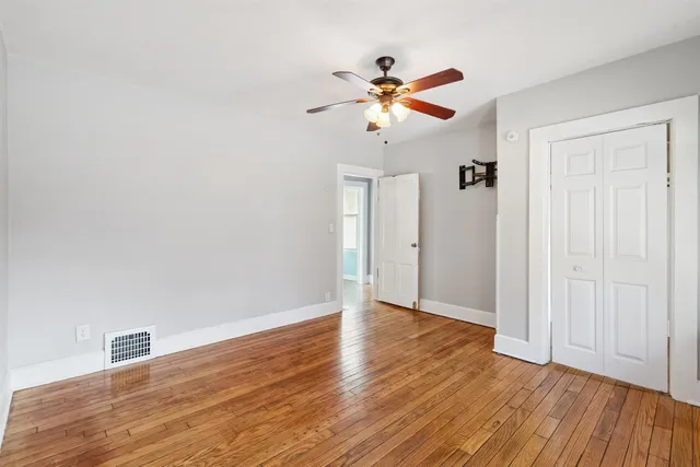 a view of an empty room with wooden floor and a ceiling fan