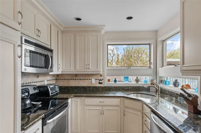 a kitchen with stainless steel appliances granite countertop white cabinets sink and window