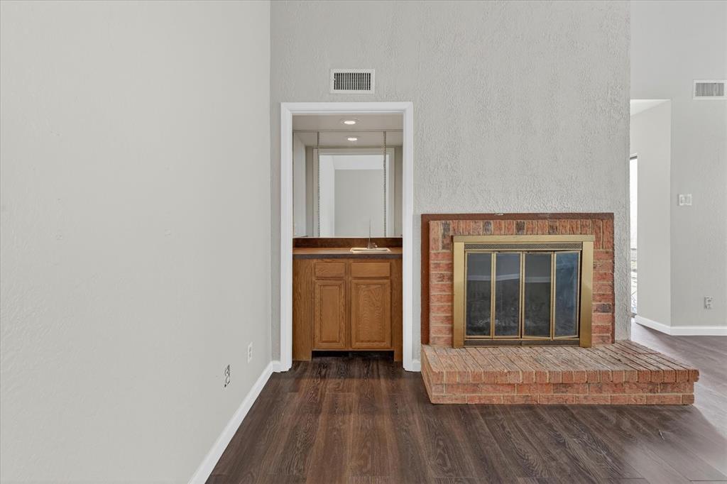 9809 Matchpoint Place Dallas, TX 75243 - Photo 5 of 21 Brick fireplace with a brass firebox, hearth, built-in wet bar, wood-finish flooring, and light-toned walls