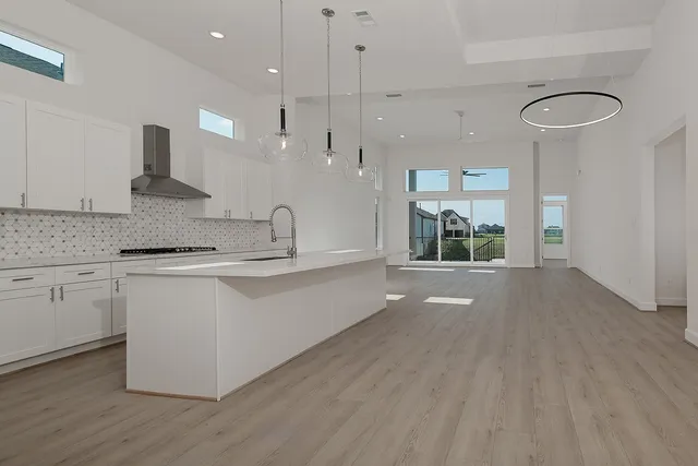 a open kitchen with granite countertop a stove top oven a sink and white cabinets with wooden floor