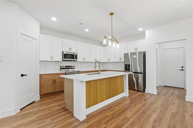 a kitchen with stainless steel appliances granite countertop a refrigerator a sink dishwasher a stove and white countertops with wooden floor