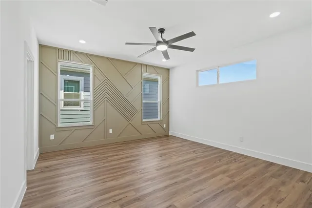 a view of an empty room with wooden floor and a ceiling fan